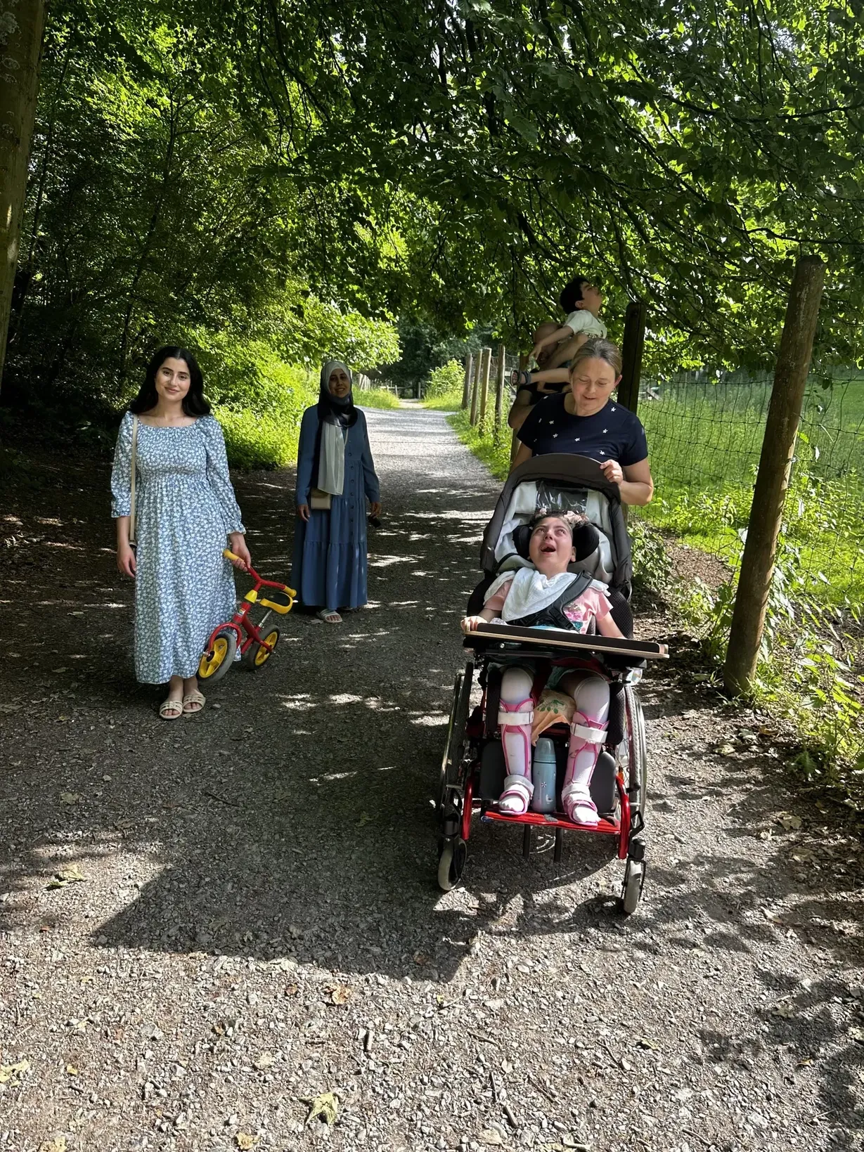 Gemeinsamer Spaziergang im Grünen mit einem Kind im Rollstuhl und Pflegekräften im Rahmen der Verhinderungspflege und außerklinischen Intensivpflege.